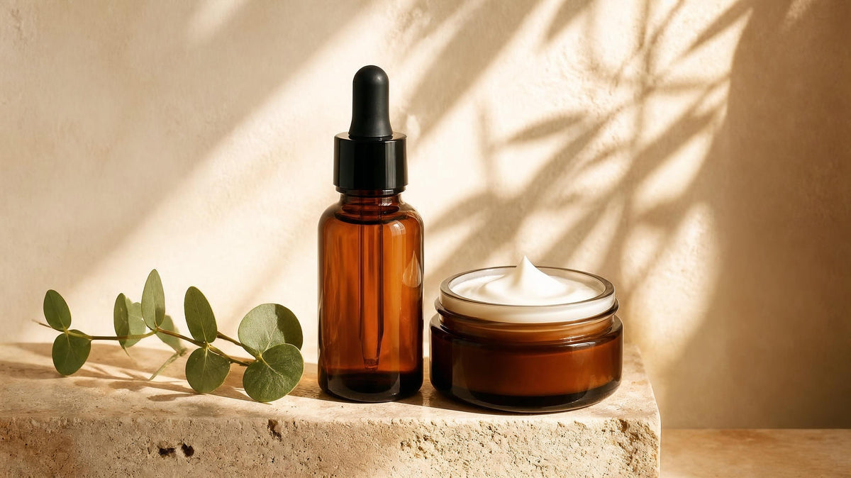 Amber dropper serum bottle beside an open jar of moisturizer cream on warm travertine stone